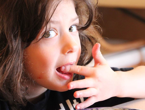 Young girl with brown hair licking her fingertips